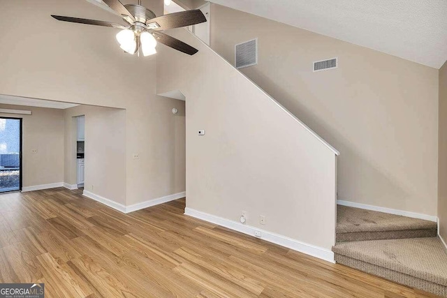 unfurnished living room with a textured ceiling, high vaulted ceiling, light wood-type flooring, and ceiling fan