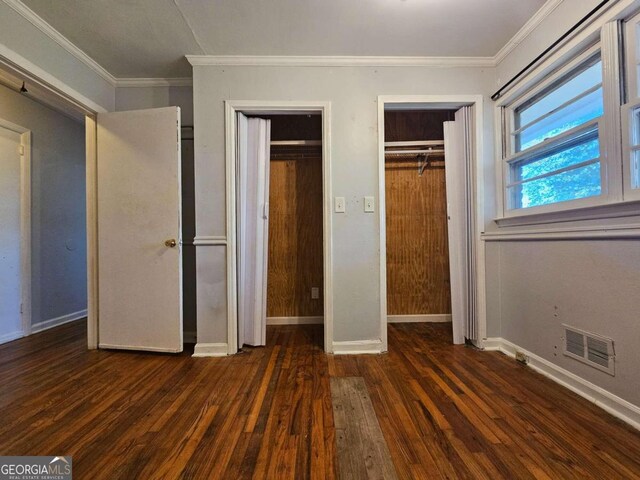 unfurnished bedroom with crown molding, two closets, and dark hardwood / wood-style floors