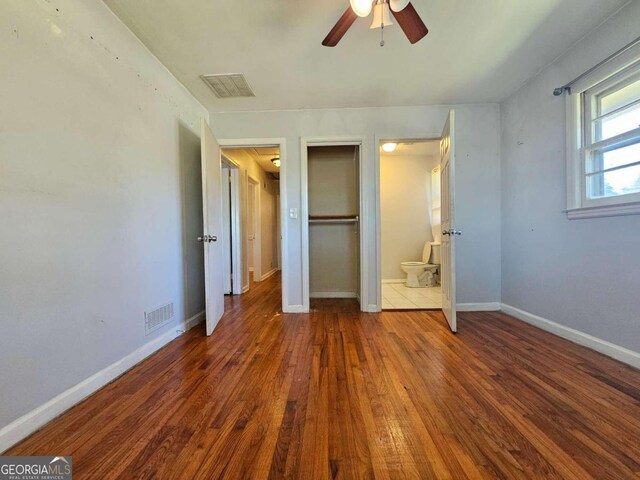 unfurnished bedroom with dark wood-type flooring, ensuite bath, and ceiling fan