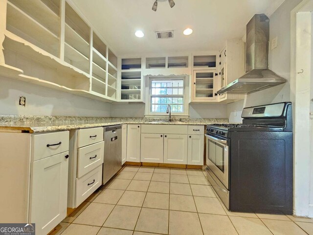 kitchen featuring wall chimney range hood, stainless steel appliances, sink, light tile patterned flooring, and white cabinets