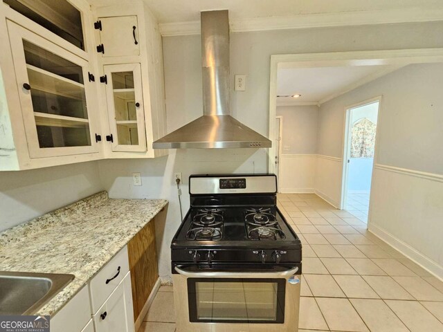 kitchen featuring light tile patterned floors, white cabinetry, ornamental molding, wall chimney exhaust hood, and stainless steel range with gas cooktop