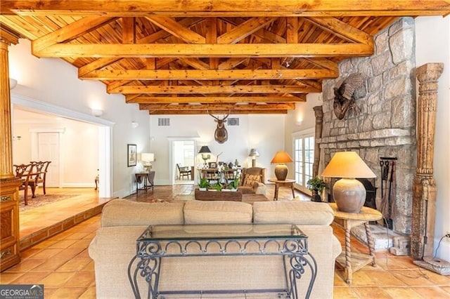 living room featuring beam ceiling, a stone fireplace, wooden ceiling, and light tile patterned floors