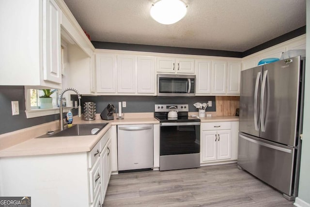 kitchen featuring appliances with stainless steel finishes, white cabinetry, a textured ceiling, light hardwood / wood-style flooring, and sink