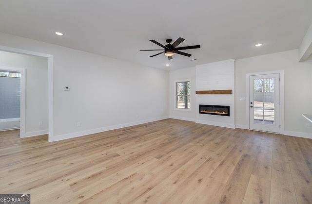 unfurnished living room with ceiling fan, a large fireplace, and light hardwood / wood-style flooring