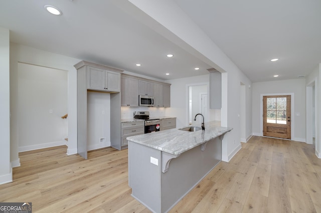 kitchen featuring sink, light wood-type flooring, light stone counters, a breakfast bar area, and stainless steel appliances