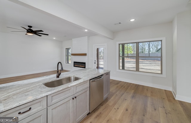 kitchen featuring dishwasher, a fireplace, light hardwood / wood-style floors, sink, and light stone counters