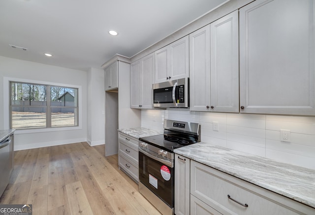 kitchen featuring light wood-type flooring, tasteful backsplash, gray cabinetry, light stone counters, and stainless steel appliances