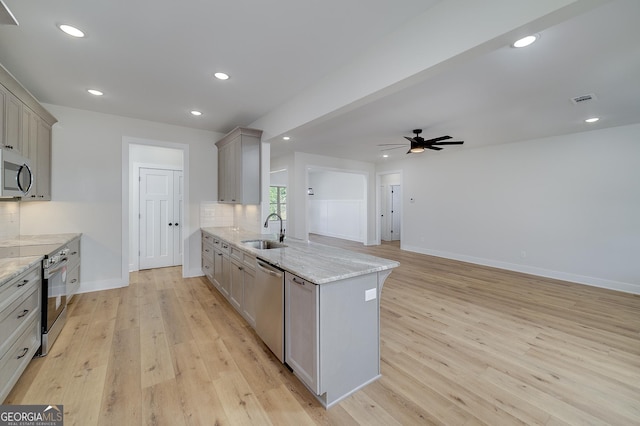 kitchen with light stone countertops, stainless steel appliances, decorative backsplash, sink, and gray cabinetry