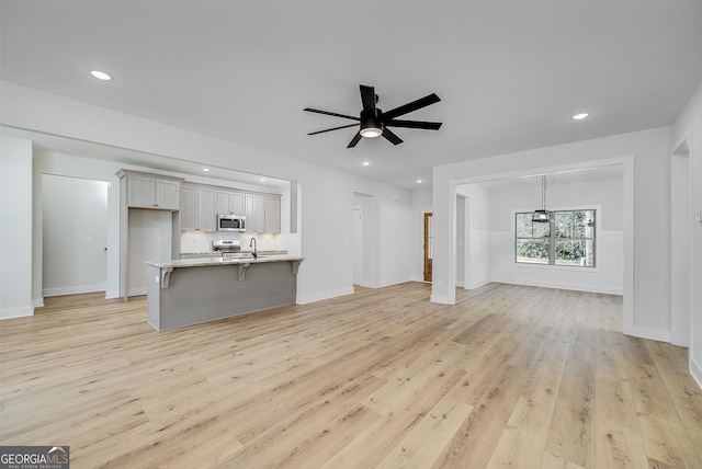 unfurnished living room with sink, light hardwood / wood-style floors, and ceiling fan