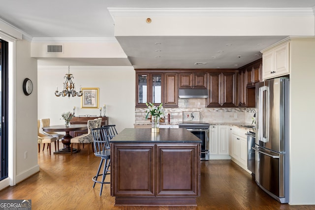 kitchen with under cabinet range hood, stainless steel appliances, visible vents, dark countertops, and glass insert cabinets