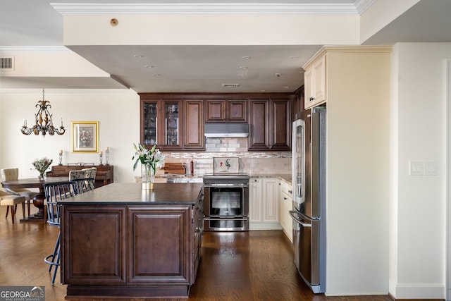 kitchen with dark countertops, glass insert cabinets, dark wood-type flooring, appliances with stainless steel finishes, and under cabinet range hood