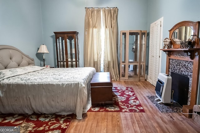 bedroom featuring heating unit, wood-type flooring, and a tile fireplace