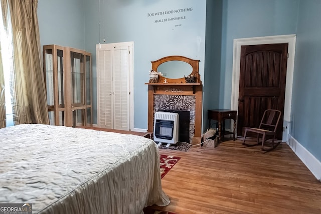 bedroom with wood-type flooring, a high ceiling, and heating unit