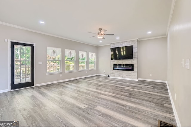 unfurnished living room with a tiled fireplace, a wealth of natural light, wood-type flooring, and ornamental molding