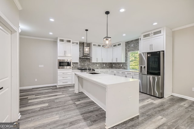 kitchen with appliances with stainless steel finishes, wall chimney exhaust hood, a center island with sink, and white cabinets