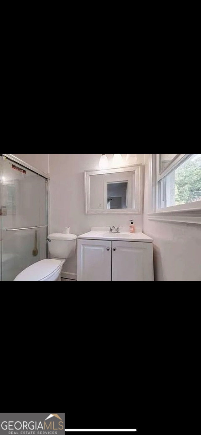 bathroom featuring a shower with door, vanity, and toilet