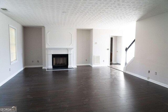 unfurnished living room with a textured ceiling and dark hardwood / wood-style flooring