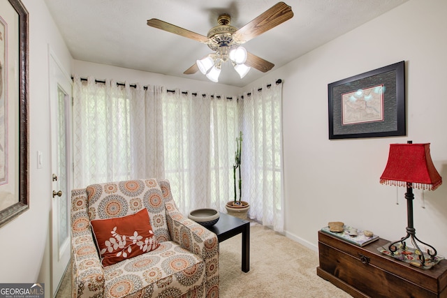 living area with ceiling fan, light carpet, and plenty of natural light