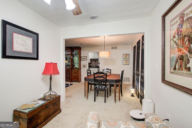 dining room featuring a textured ceiling, light colored carpet, and ceiling fan