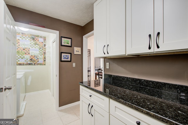 kitchen featuring white cabinets, a textured ceiling, light tile patterned floors, and dark stone countertops