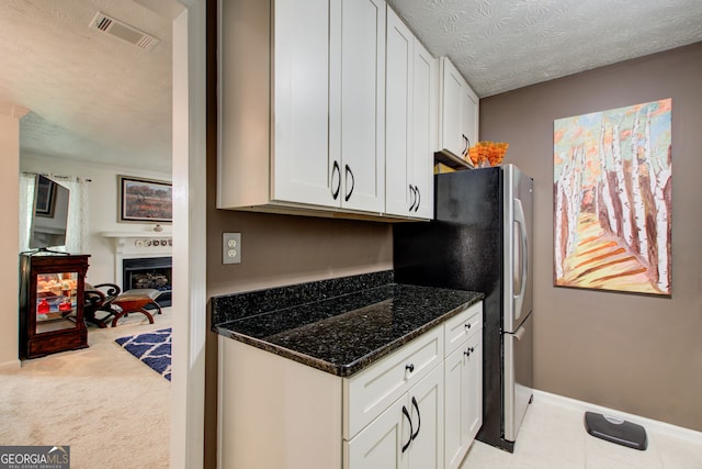 kitchen with light carpet, a textured ceiling, dark stone counters, and white cabinets