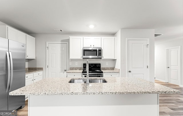 kitchen with stainless steel appliances, white cabinetry, light hardwood / wood-style floors, and an island with sink