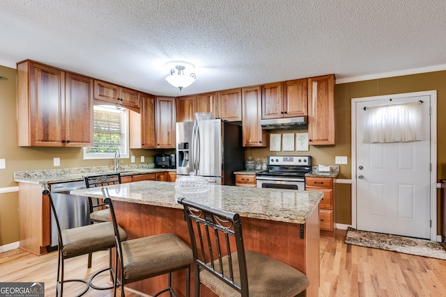 kitchen with a kitchen island, a kitchen breakfast bar, light wood-type flooring, stainless steel appliances, and light stone counters