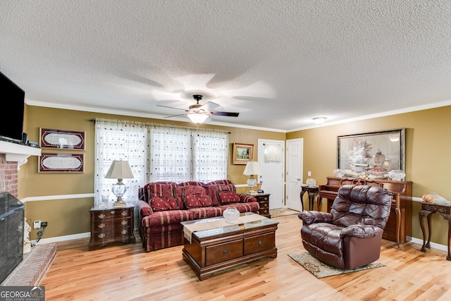 living room with light wood-type flooring, a fireplace, a textured ceiling, ceiling fan, and ornamental molding