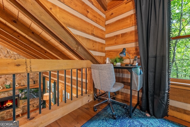 office space featuring lofted ceiling, a stone fireplace, hardwood / wood-style floors, and wood walls