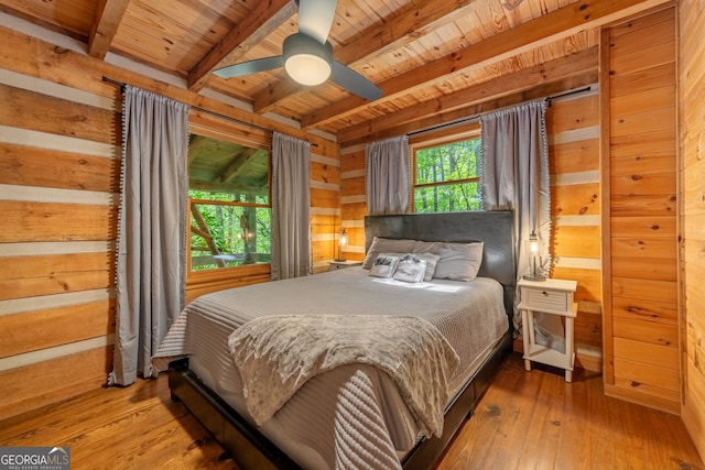 bedroom featuring wooden walls, light hardwood / wood-style floors, beamed ceiling, and ceiling fan