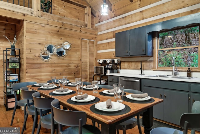 kitchen featuring stainless steel dishwasher, sink, hardwood / wood-style floors, and wood walls