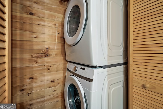 washroom featuring stacked washer / drying machine and wooden walls