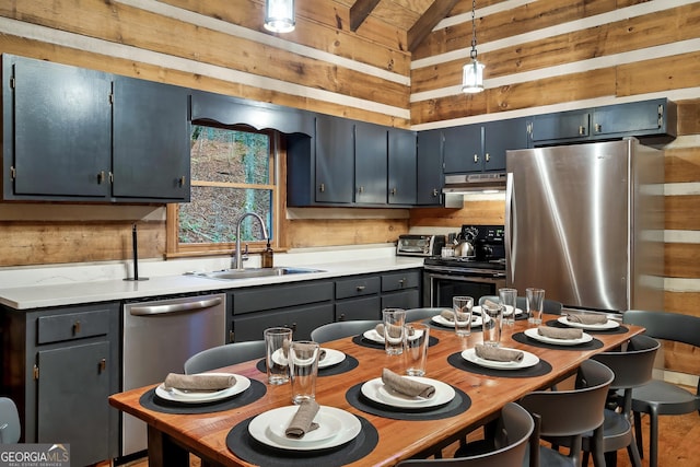 kitchen featuring sink, wood walls, lofted ceiling with beams, hanging light fixtures, and stainless steel appliances