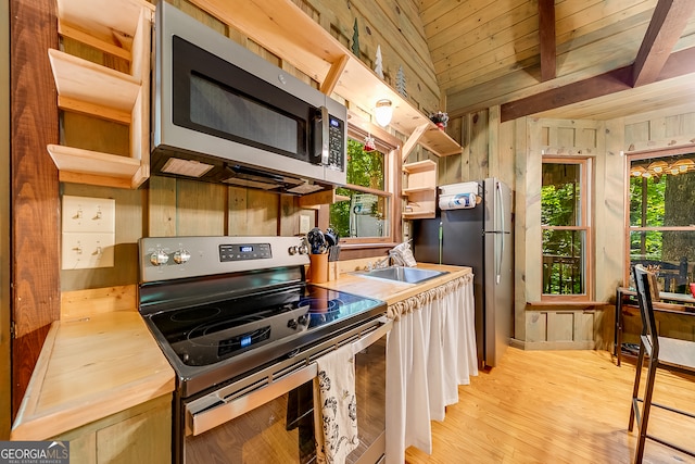 kitchen featuring appliances with stainless steel finishes, wooden ceiling, light wood-type flooring, wooden walls, and sink