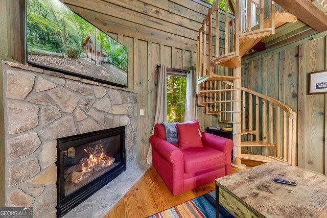 living room featuring wood walls, wood-type flooring, and a stone fireplace