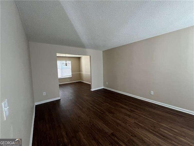 unfurnished room featuring lofted ceiling, dark wood-type flooring, a textured ceiling, and a chandelier