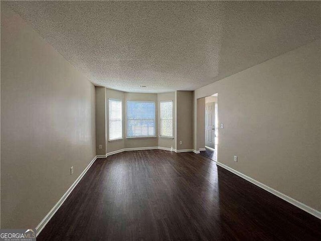 empty room with a textured ceiling and dark hardwood / wood-style flooring