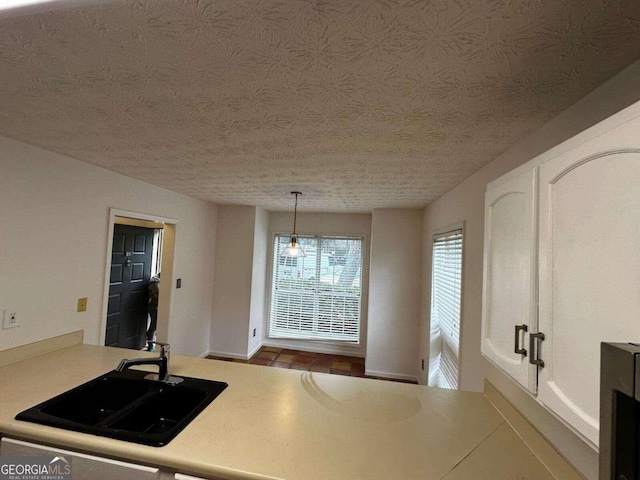 kitchen featuring sink, a textured ceiling, white cabinetry, and decorative light fixtures