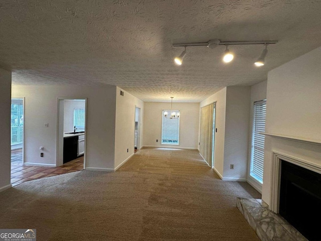 hall with track lighting, sink, light colored carpet, a chandelier, and a textured ceiling