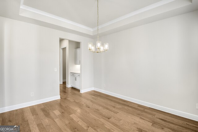 spare room featuring a raised ceiling, a chandelier, and light wood-type flooring