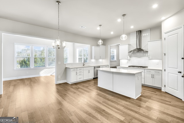 kitchen with a wealth of natural light, a center island, white cabinets, and wall chimney range hood