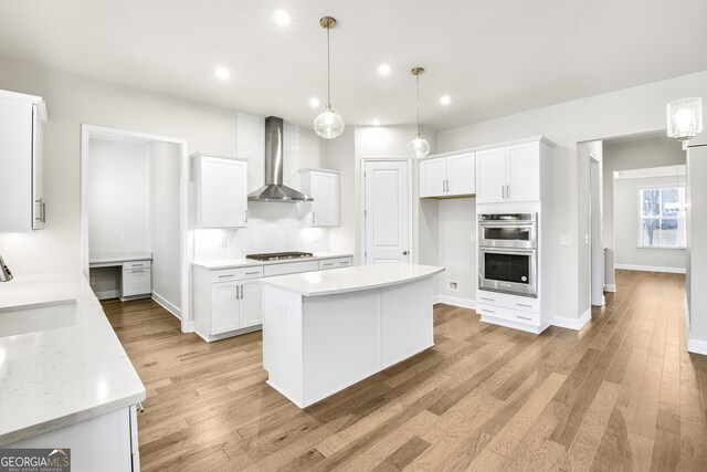 kitchen with white cabinetry, wall chimney exhaust hood, hanging light fixtures, and light hardwood / wood-style floors