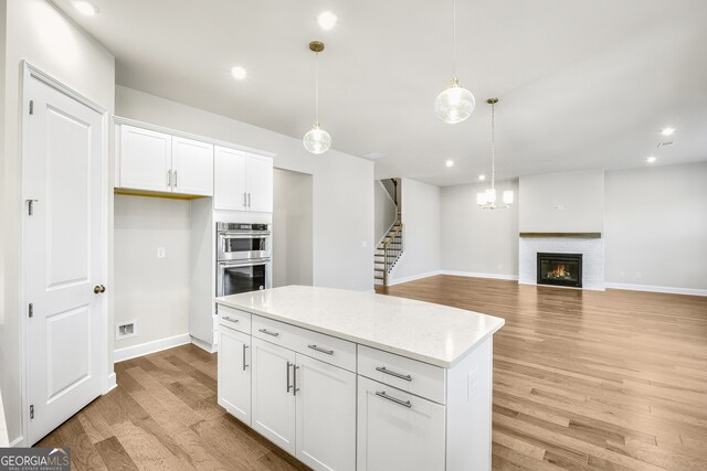 kitchen with double oven, white cabinets, light hardwood / wood-style floors, and decorative light fixtures