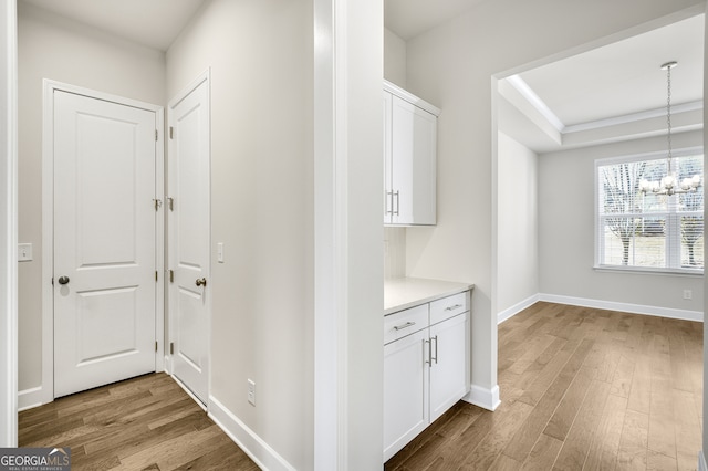 corridor with light wood-type flooring and an inviting chandelier