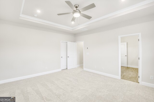 interior space featuring ceiling fan, light colored carpet, and a tray ceiling