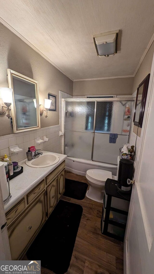 full bathroom featuring toilet, vanity, hardwood / wood-style floors, bath / shower combo with glass door, and tile walls