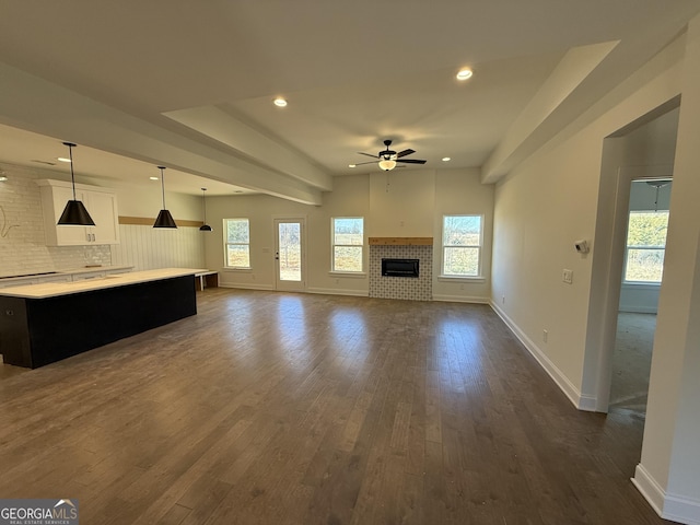 unfurnished living room with dark wood-type flooring, ceiling fan, and a wealth of natural light