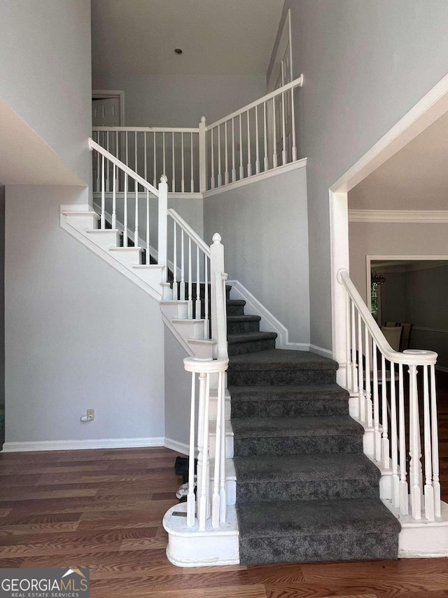 stairs featuring hardwood / wood-style floors, crown molding, and a towering ceiling