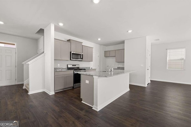 kitchen with appliances with stainless steel finishes, sink, gray cabinetry, a kitchen island with sink, and light stone counters