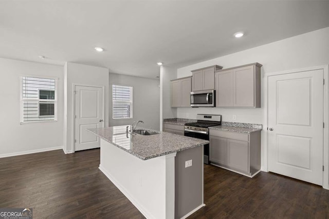 kitchen with an island with sink, sink, gray cabinetry, light stone counters, and stainless steel appliances